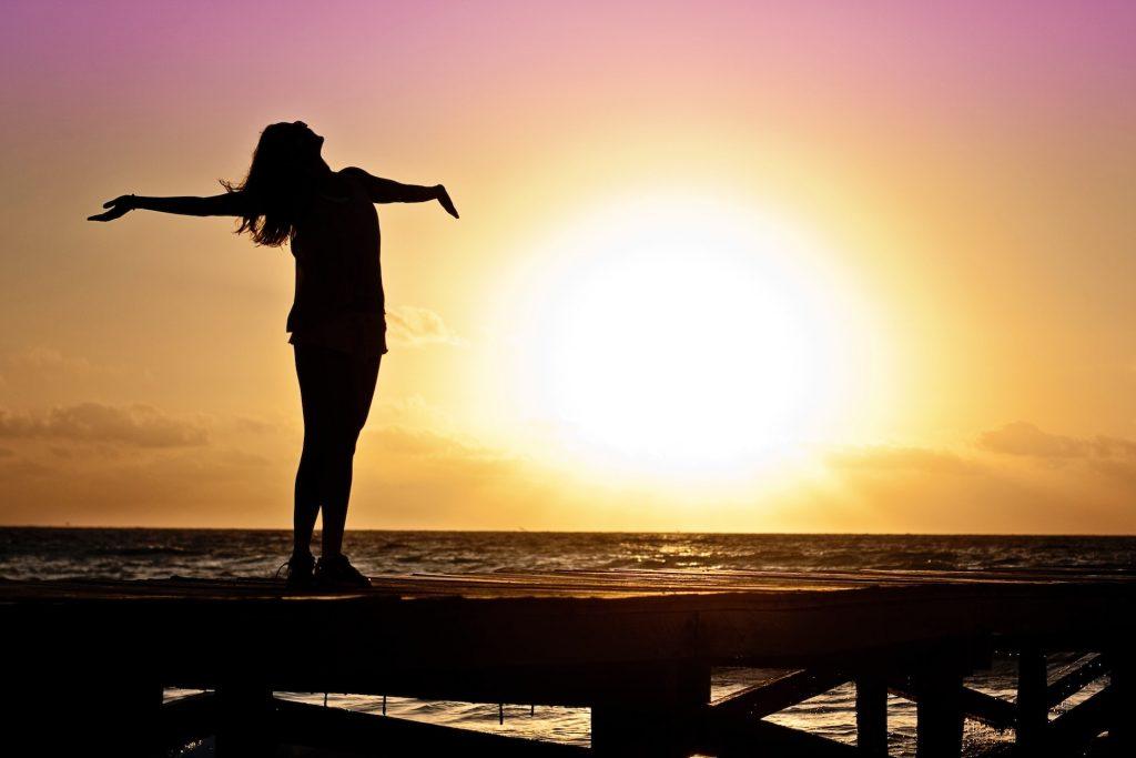 A silhouette of a woman with her arms wide open and a view of a beautiful sunset behind her.