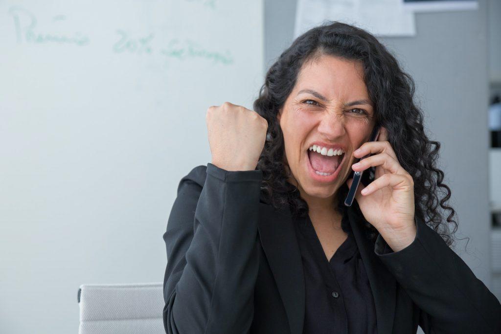 A woman talking on a phone in her office with an extremely happy expression and body language.