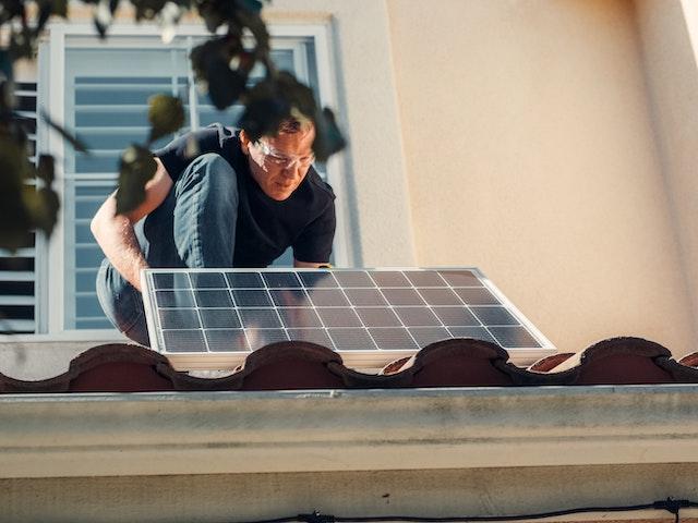 A man installing a solar panel on the roof.