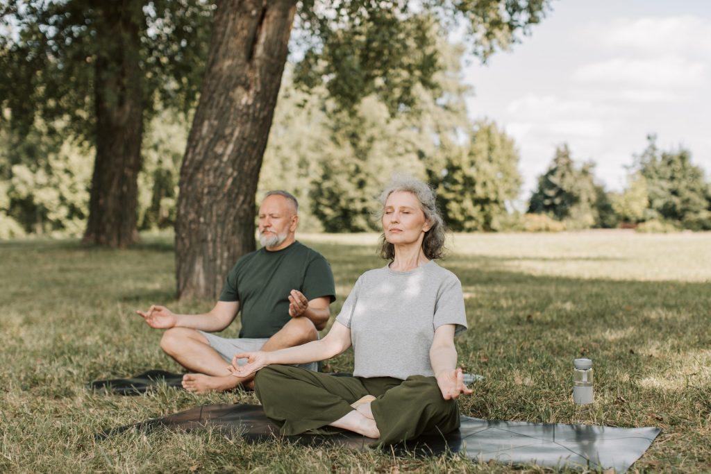 An elderly couple sitting down and meditating on a field.