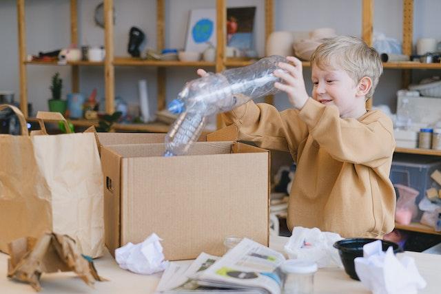 Boy putting plastic bottles into cardboard boxes as an example of recycling