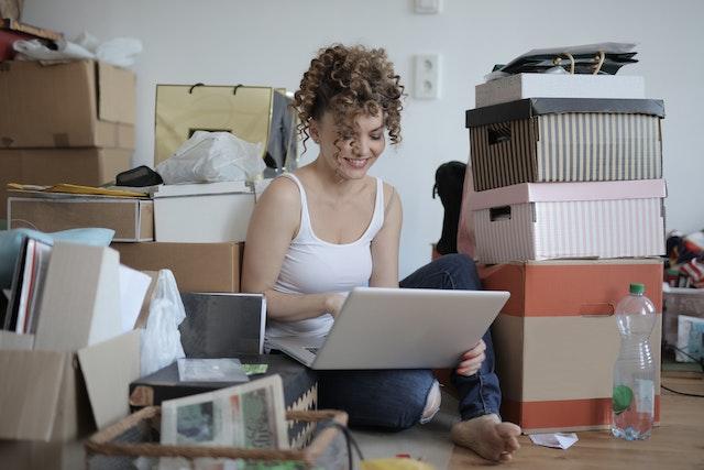 Woman sitting on the floor and using a laptop surrounded by clutter