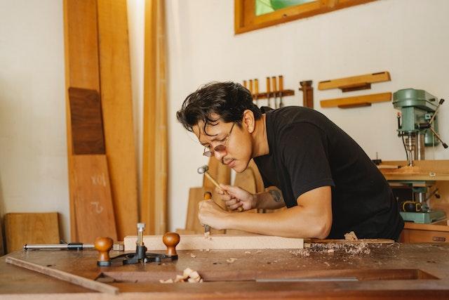 A man in a black t-shirt working on a piece of wood.