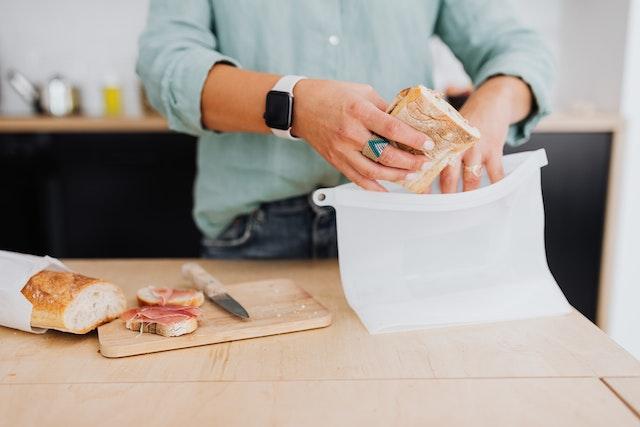 a person packing a sandwich in a white silicone bag
