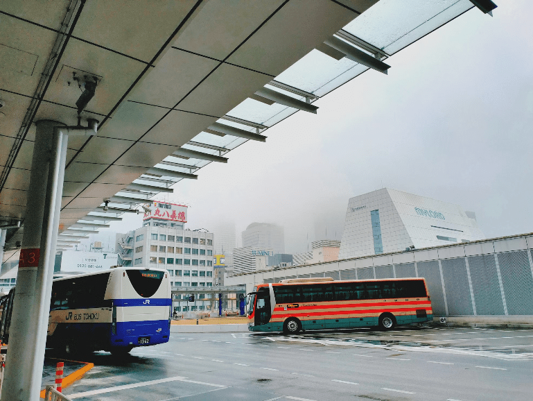 A solar bus stop in Tokyo, with a red and a blue bus near it.