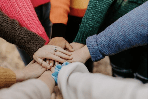 People in colorful sweaters standing in a circle with their hands together.