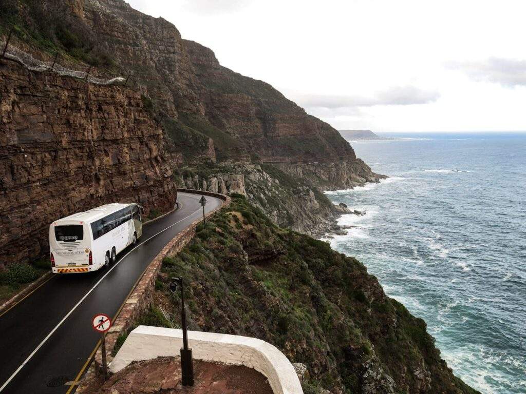 White bus on a road near a cliffside with water.