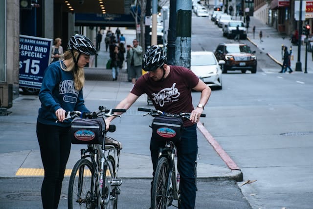 Two cyclists checking their bikes at a city intersection with bike helmets and urban traffic